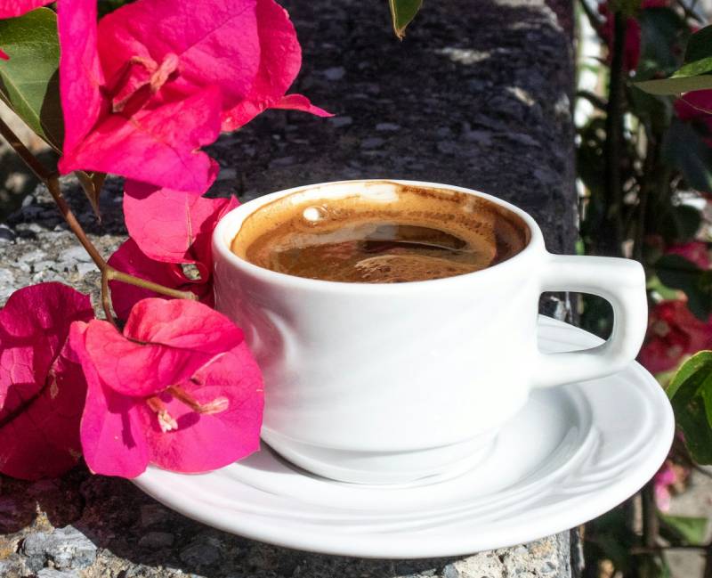 Biała filiżanka kawy wśród kwiatów